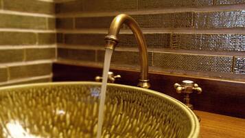 A large, ornate brass faucet with water flowing into a textured, bowl-shaped basin.