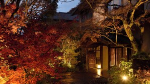 A traditional Japanese garden with a stone pathway leading to a wooden gate, surrounded by vibrant autumn foliage.