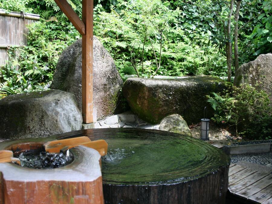 Un jardín japonés tradicional con un puente de madera, rocas grandes y una cuenca de piedra circular.