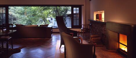 A modern living room with a fireplace, wooden flooring, and a large window overlooking a garden.