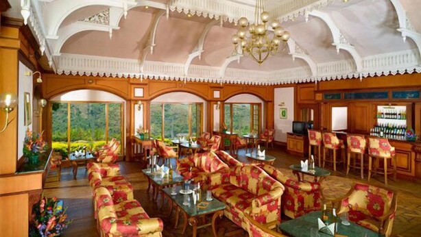 A spacious hotel lobby with ornate ceiling details, multiple seating areas, and large windows offering a view of the outdoors. - KTDC Tea County Munnar (Devikolam)