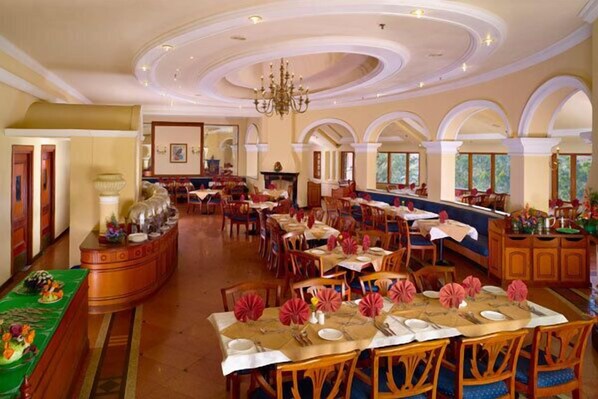 A spacious dining area with multiple tables, chandeliers, and a view of the outdoors.