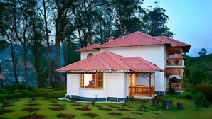 A two-story house with a red-tiled roof, surrounded by a lush garden with square plots. - KTDC Tea County Munnar (Devikolam)