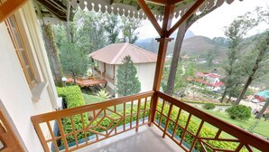 A balcony with a wooden railing overlooking a lush garden and a distant view of a village with red-roofed houses. - KTDC Tea County Munnar (Devikolam)