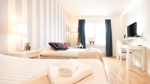A hotel room with two beds, a desk, a TV, and a window with curtains. - Attendo Park Hotell (Huddinge)