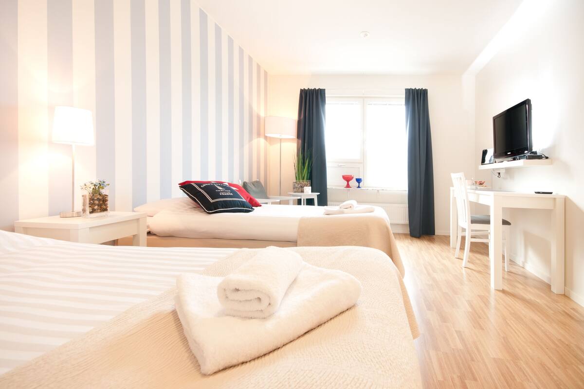 A hotel room with two beds, a desk, a TV, and a window with curtains.