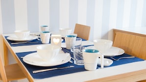 A dining table set with white dishes, blue napkins, and clear glasses, against a striped wall. - Attendo Park Hotell (Huddinge)