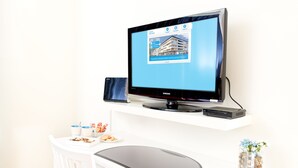 A Samsung TV on a white desk with a laptop, a small speaker, and a glass of water. - Attendo Park Hotell (Huddinge)