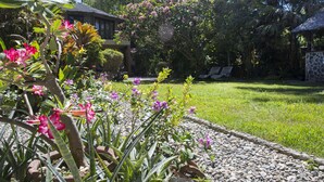Un jardín con palmeras, césped y un edificio con techo de paja.