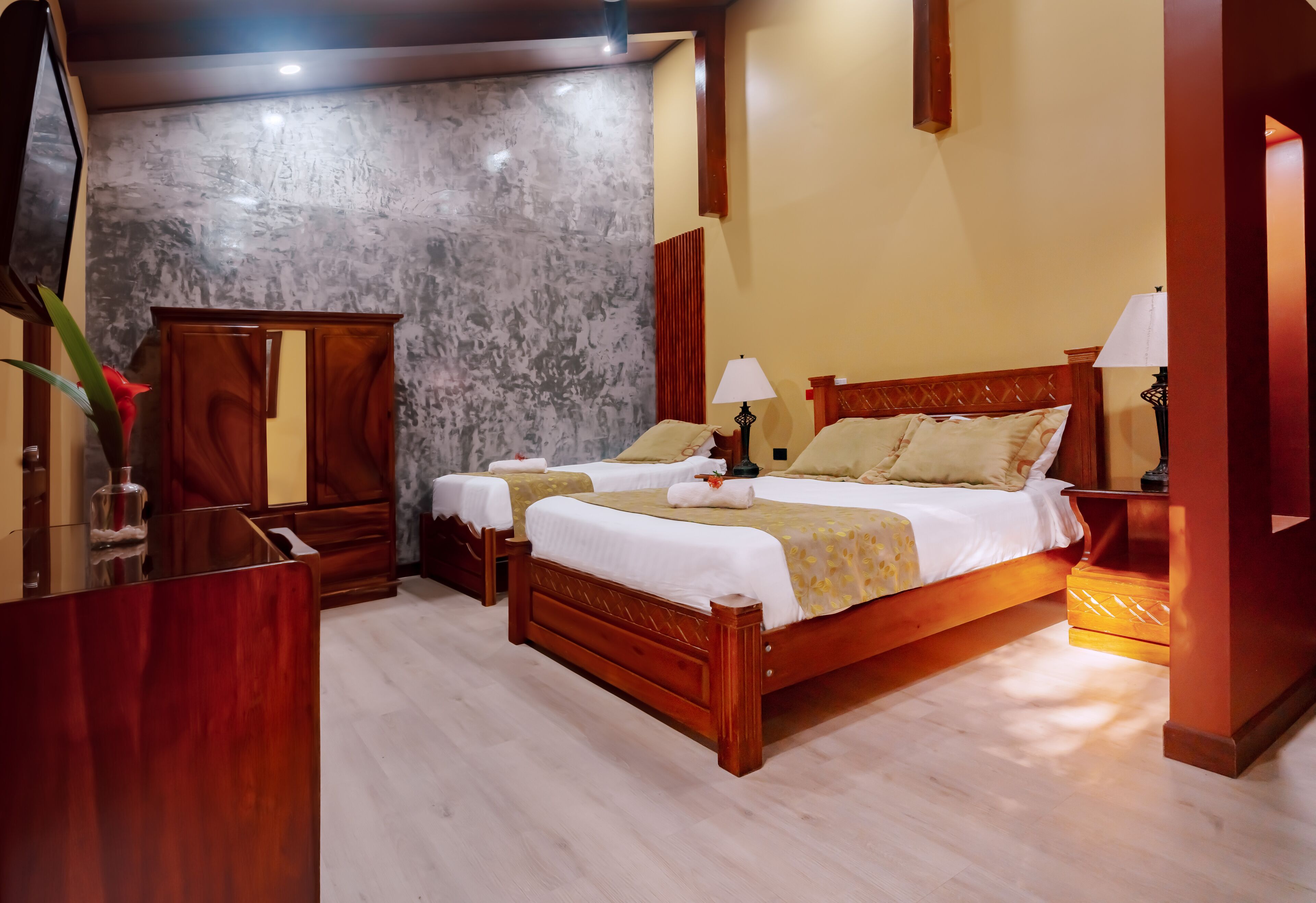 Una habitación de hotel con una cama de madera, dos mesitas de noche, un espejo y un armario.