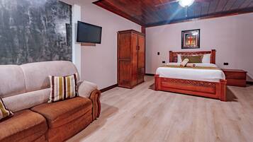 A bedroom with a wooden ceiling, a bed with a headboard, a wooden wardrobe, a flat-screen TV, and a couch.