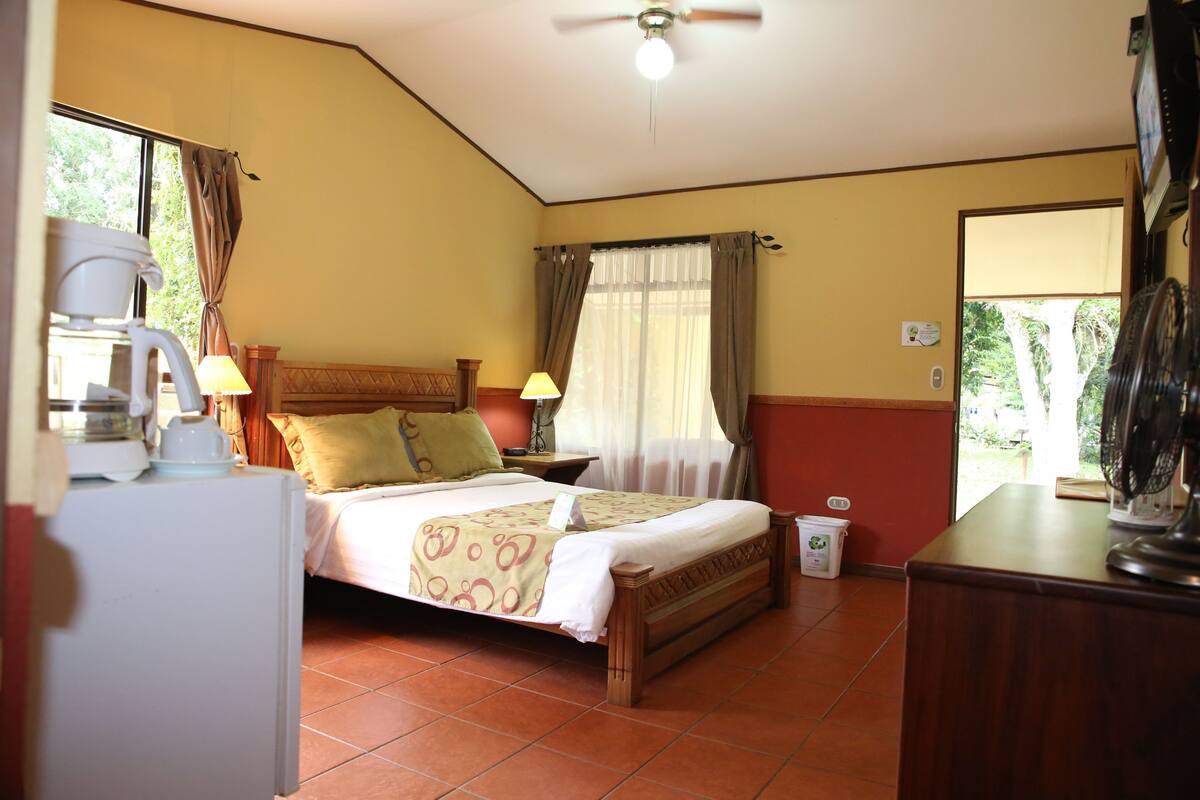 A bedroom with a bed, a nightstand, a lamp, a ceiling fan, and a window with curtains.