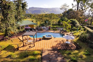 Una piscina con hidromasaje, rodeada de un patio con mobiliario exterior, con un telón de fondo de exuberante vegetación y montañas.