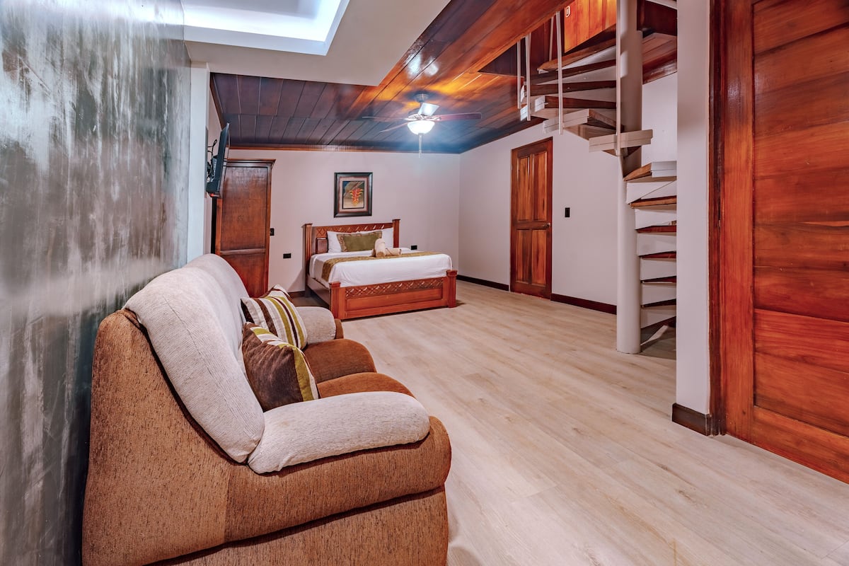 A room with a wooden ceiling, a bed, a sofa, and a staircase.