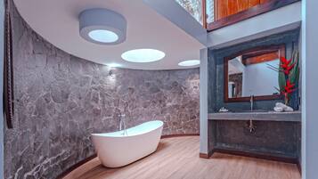 A modern bathroom with a freestanding bathtub, stone walls, and a wooden floor.