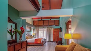 A hotel room with a bed, a sofa, a wooden dresser, a mirror, and a window with curtains. - Hotel Villa Florencia (Turrialba)