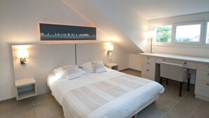 A bedroom with a bed, bedside tables, a desk, and a window.