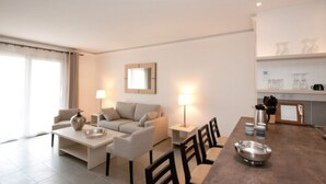 A modern living room with a sofa, coffee table, and dining area. There is a kitchen area with a countertop and cabinets.