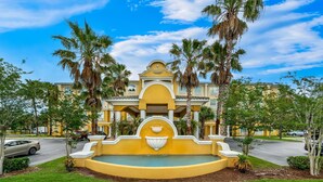 A hotel with a fountain, palm trees, and a clear blue sky. - Country Inn & Suites by Radisson, Port Orange-Daytona, FL (Port Orange)