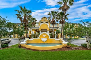 A hotel with a fountain, palm trees, and a clear blue sky. - Country Inn & Suites by Radisson, Port Orange-Daytona, FL (Port Orange)