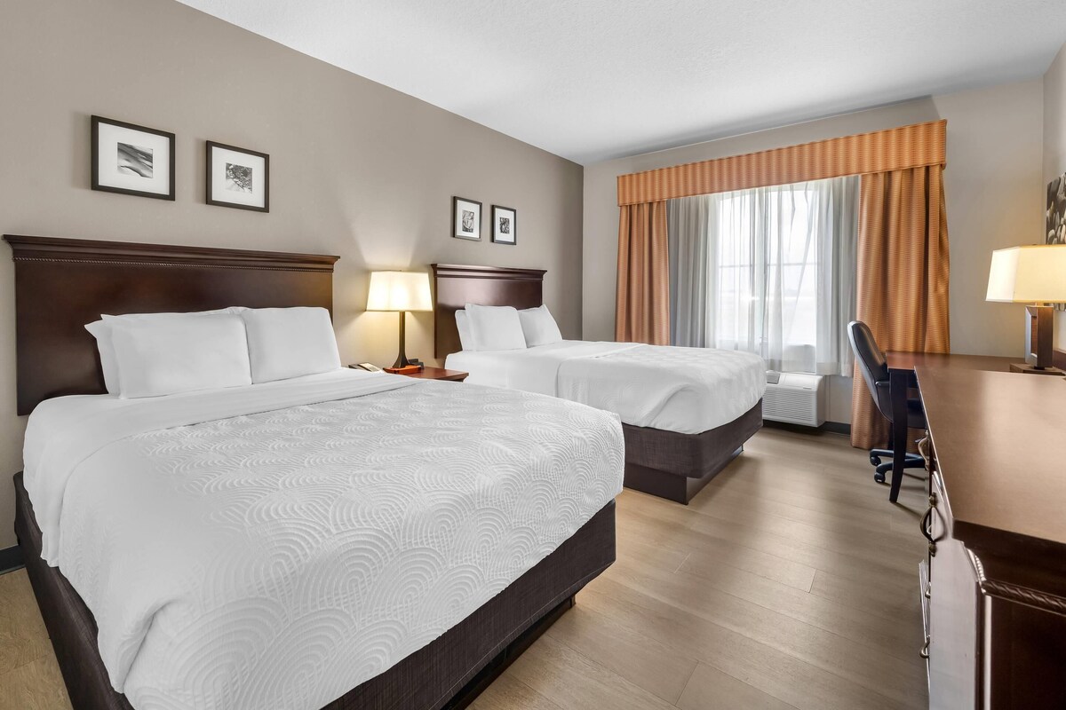 Een hotelkamer met twee bedden, een bureau, een stoel en een raam met gordijnen.
