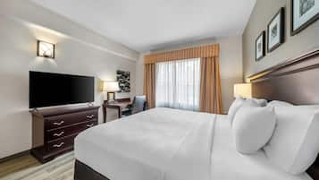 A hotel room with a large bed, a flat-screen TV, a desk with a chair, and a window with curtains.