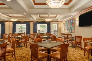 A hotel dining area with multiple tables and chairs, large windows, and a painting on the wall. - Country Inn & Suites by Radisson, Port Orange-Daytona, FL (Port Orange)