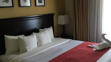 A neatly made bed with white linens and a red accent, a dark headboard, and three framed pictures on the wall.