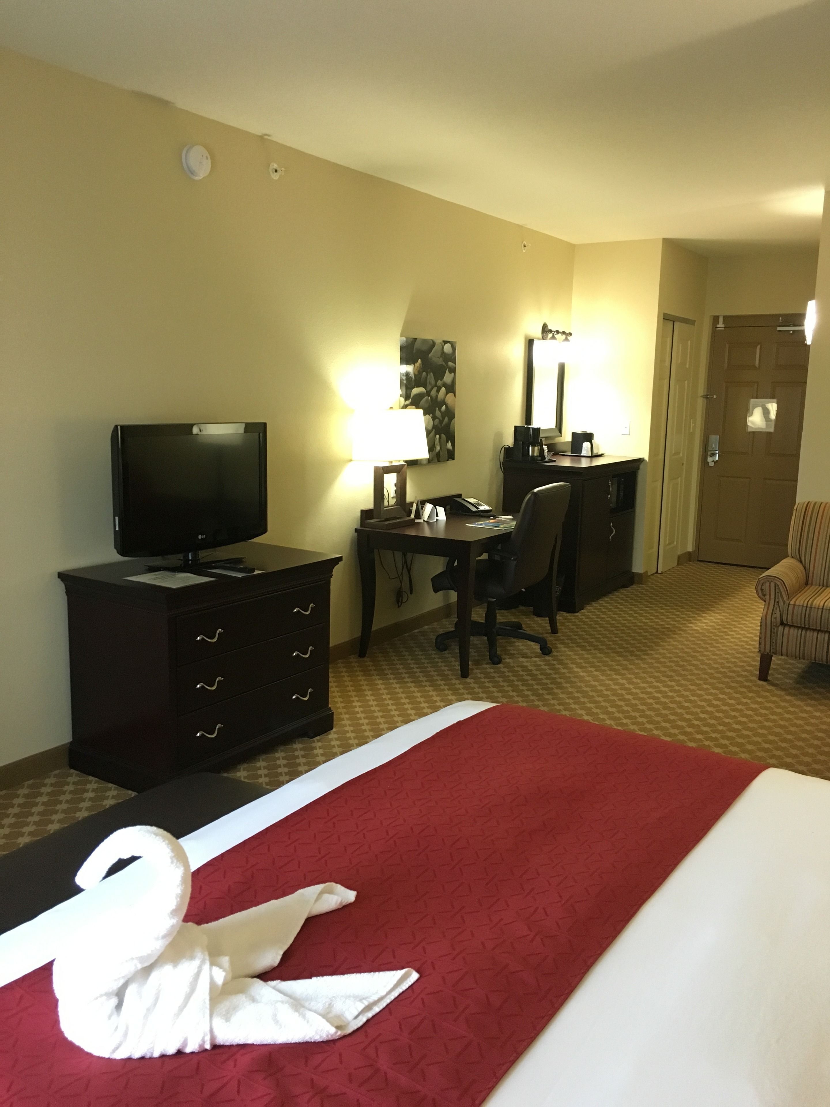 A hotel room with a bed, a desk, a chair, a television, and a lamp.