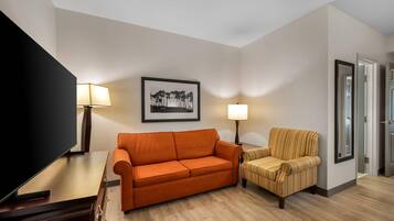 A living room with a sofa, armchair, TV, and lamps.