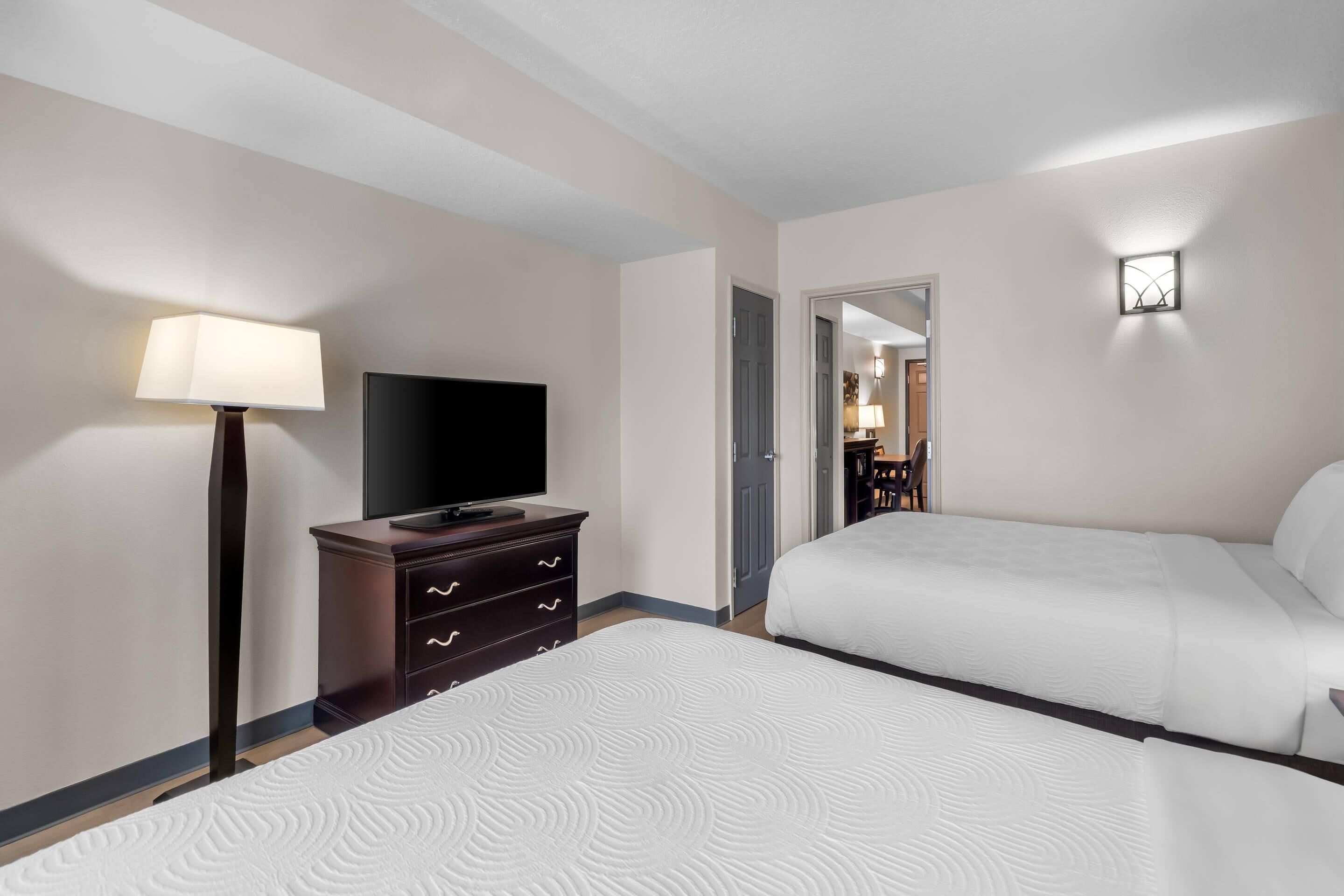Una habitación de hotel con una cama, televisión, cómoda y lámpara.