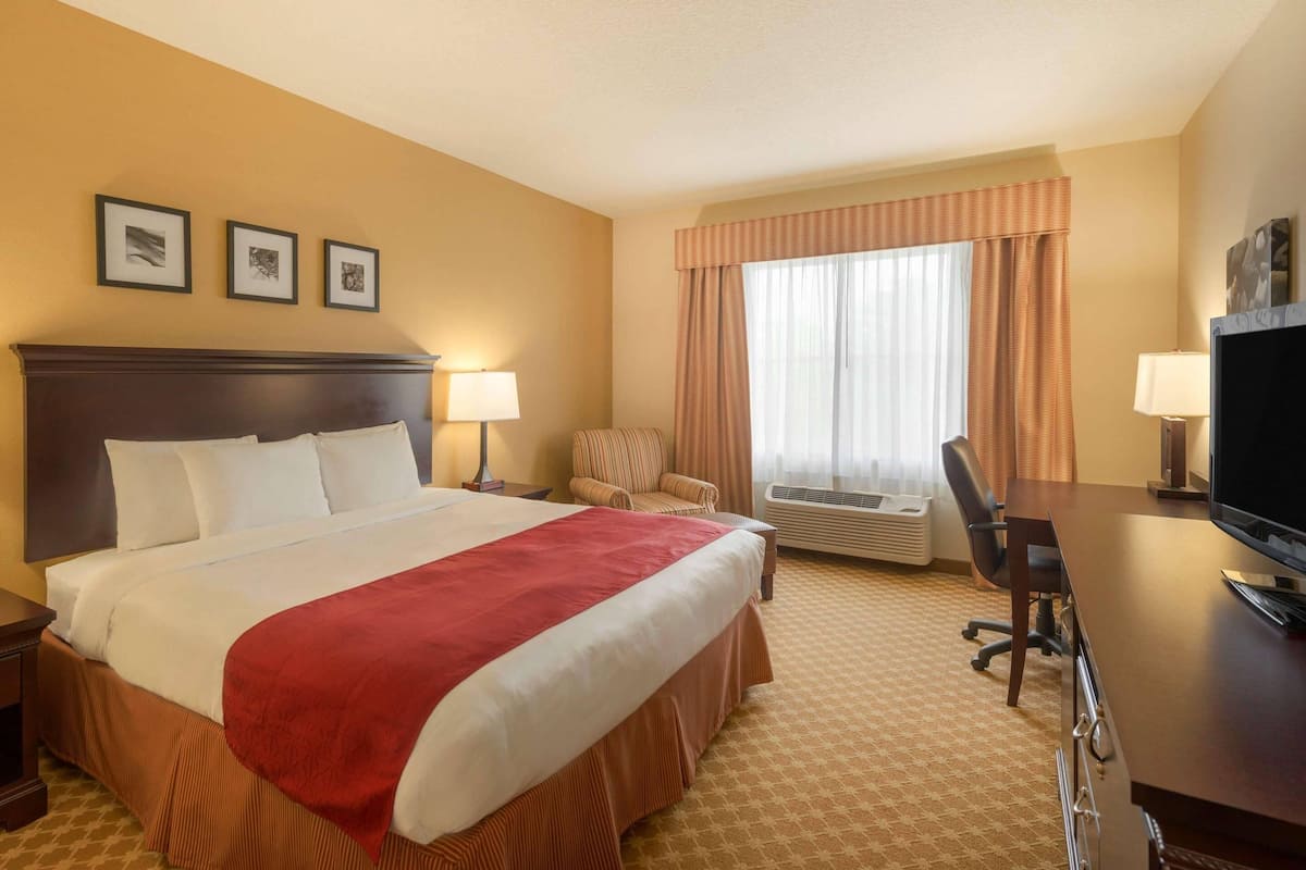 Habitación de hotel con una cama grande, un escritorio con computadora, aire acondicionado, una silla y cuadros en la pared.