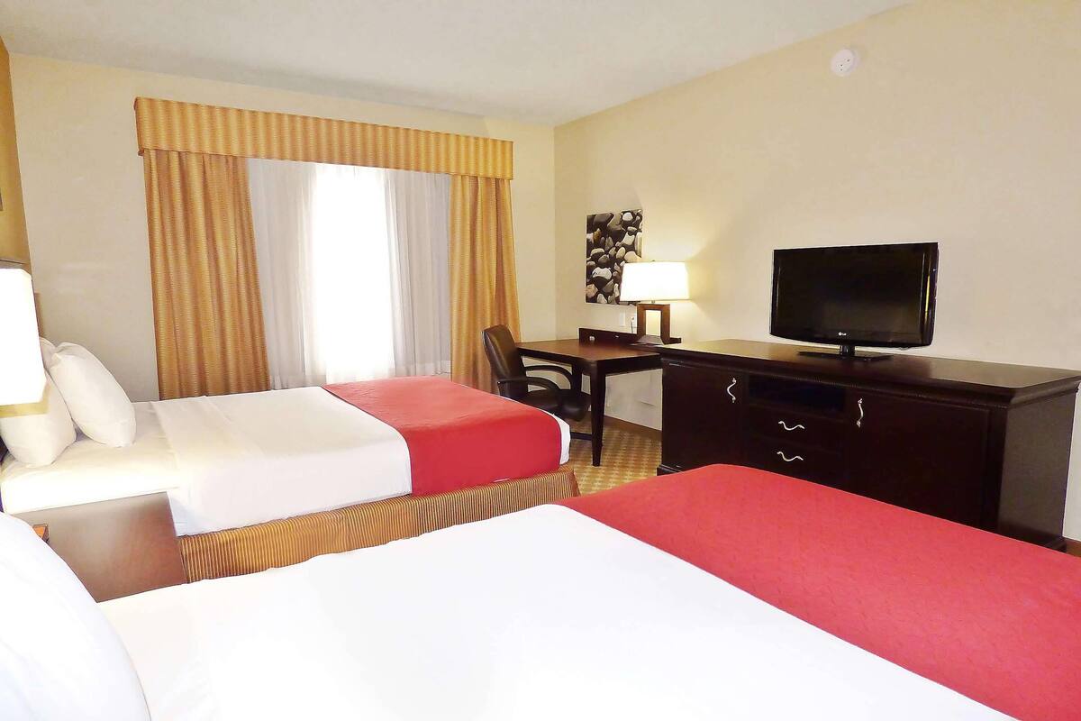 A hotel room with two beds, a desk, a television, and a lamp.