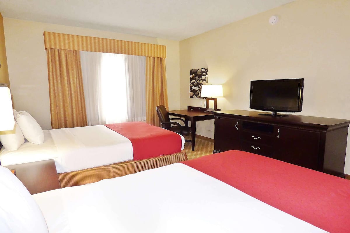 Una habitación de hotel con dos camas, un escritorio, un televisor y una lámpara.