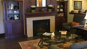 A living room with a fireplace, a bookshelf, a coffee table, and a sofa. - Country Inn & Suites by Radisson, Port Orange-Daytona, FL (Port Orange)