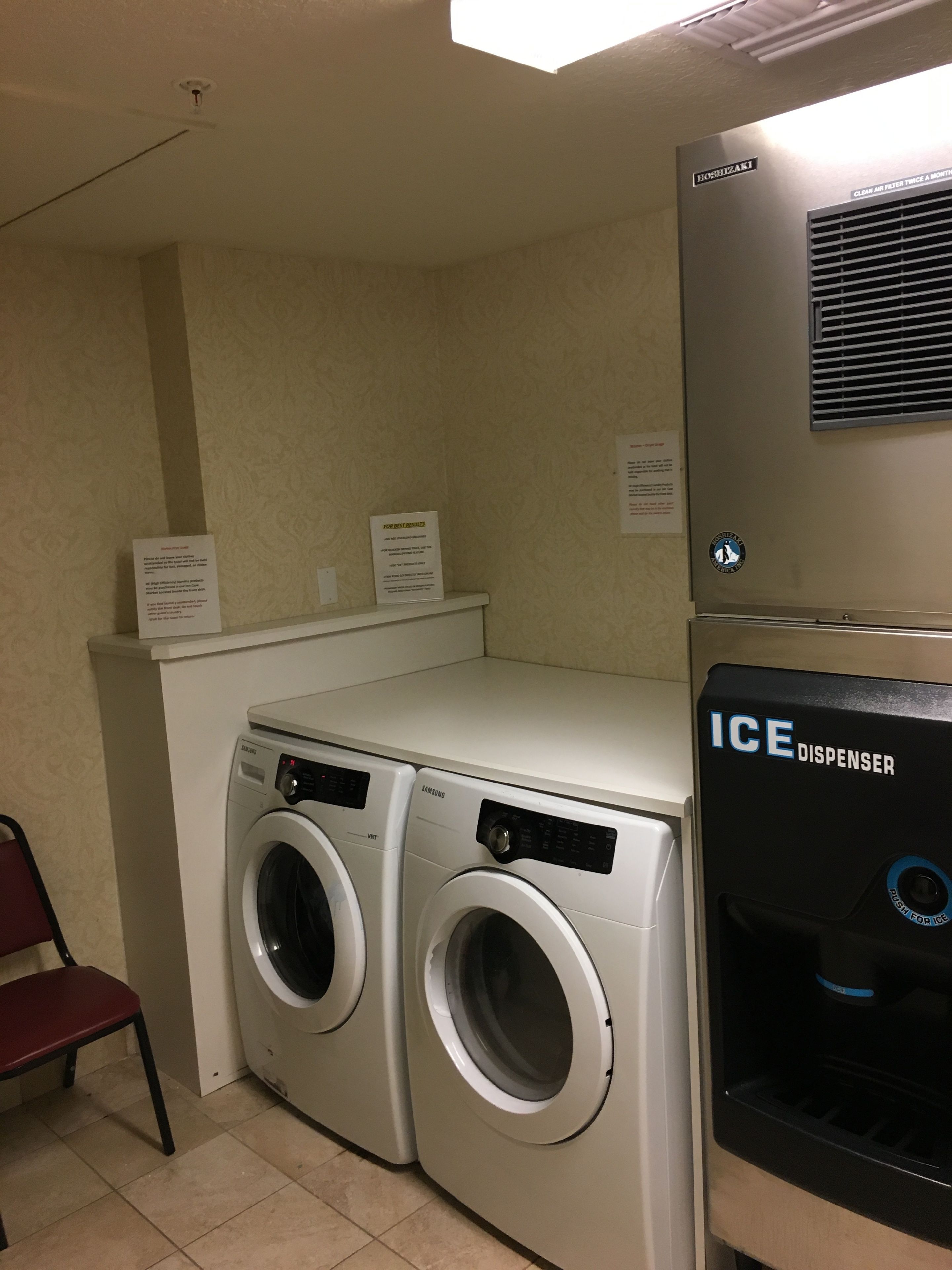 A laundry area with two Samsung washing machines, an ice dispenser, and a chair.