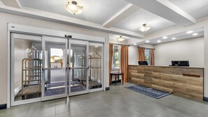 A reception area with a wooden reception desk, a glass door entrance, and a welcome mat. - Country Inn & Suites by Radisson, Port Orange-Daytona, FL (Port Orange)
