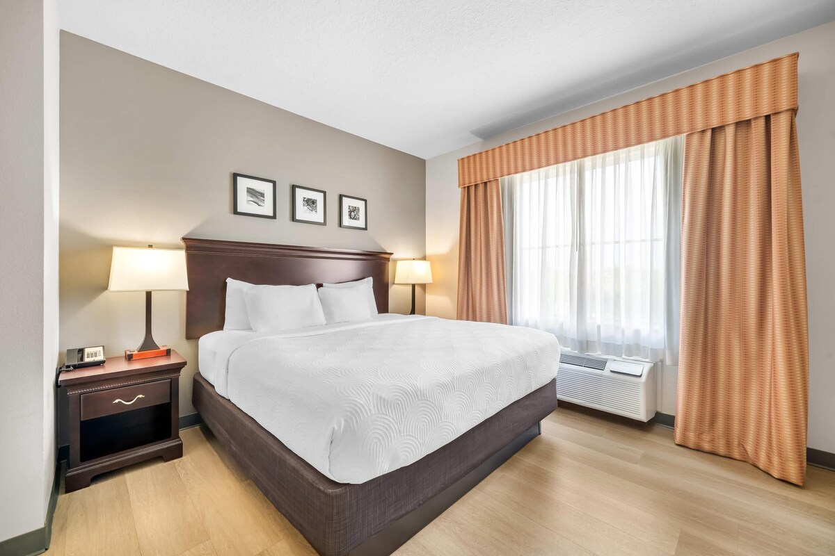 Hotelkamer met een groot bed, twee nachtkastjes met lampen, een wandairconditioner en een raam met gordijnen.