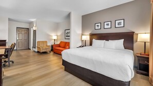 A hotel room with a large bed, a desk, an orange chair, and a door leading to another room. - Country Inn & Suites by Radisson, Port Orange-Daytona, FL (Port Orange)