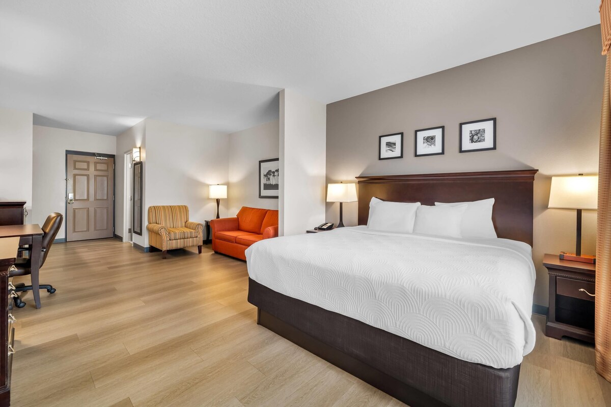 Een hotelkamer met een groot bed, een bureau, een oranje stoel en een deur naar een andere kamer.