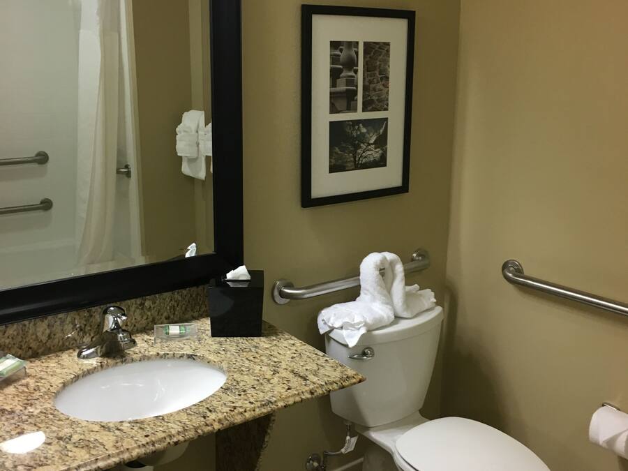 A bathroom with a sink, mirror, toilet, and a framed picture on the wall.