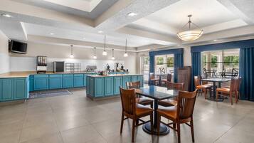 A spacious kitchen with blue cabinets, a central island, and a dining area with wooden chairs and a table.
