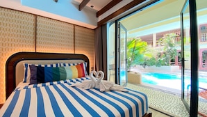 Habitación de hotel con una cama grande, ropa de cama a rayas y vistas a una piscina y zona exterior.