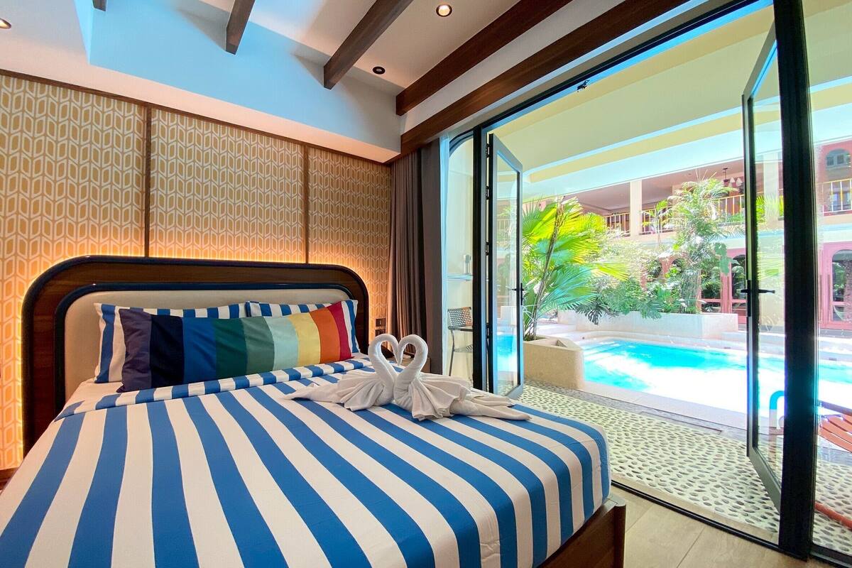 A hotel room with a large bed, striped bedding, and a view of a pool and outdoor area.