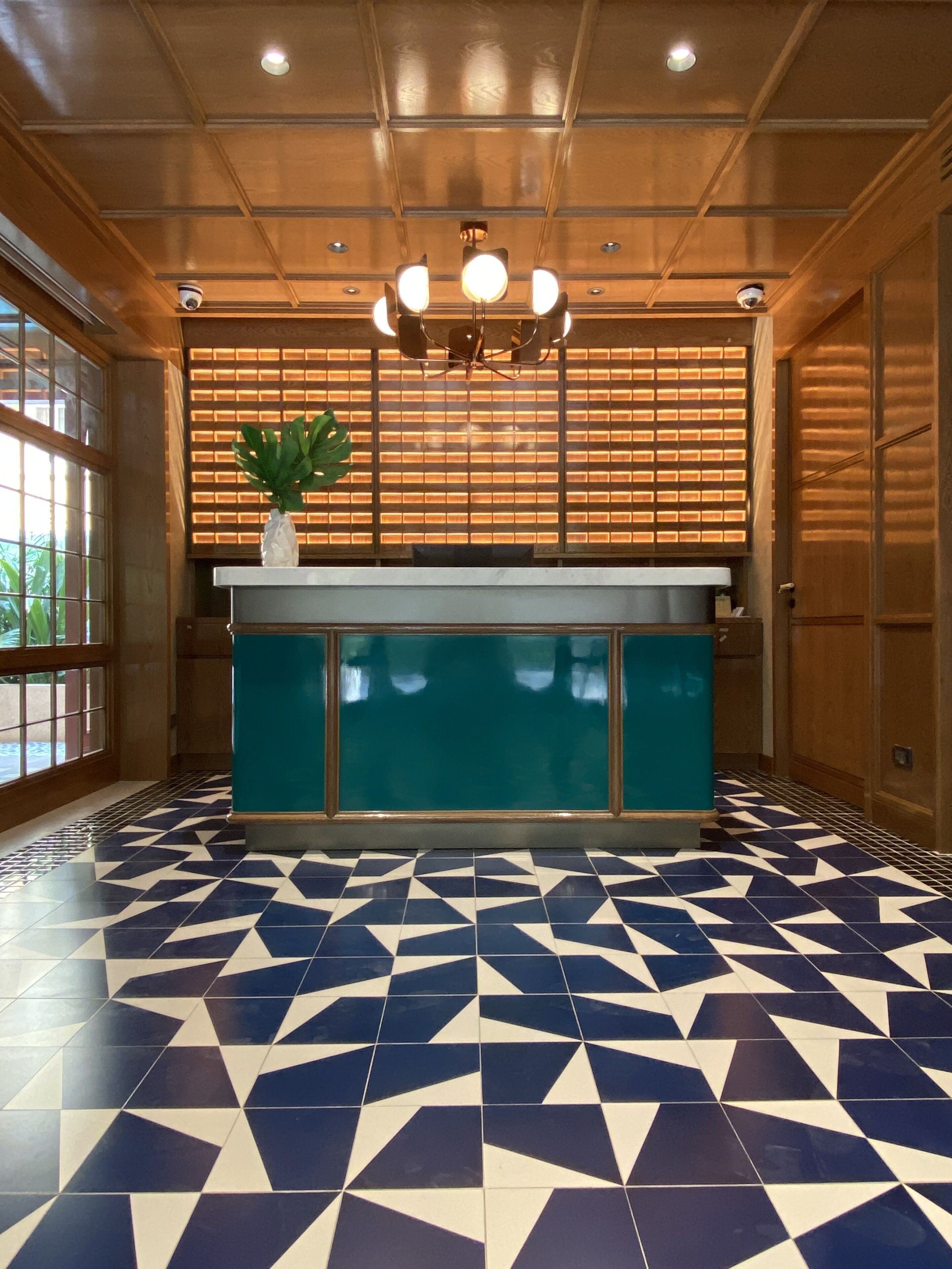 Una zona de recepción con mostrador azul aguamarina, baldosas de suelo estampadas y techo de madera con iluminación empotrada.