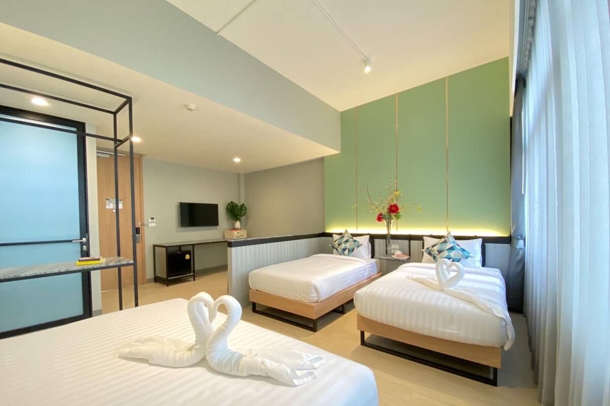 A hotel room with two beds, a TV, a desk, and a plant.