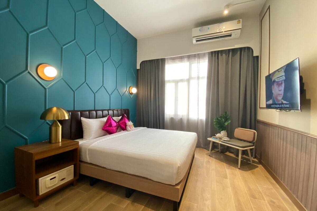 A modern hotel room with a large bed, a TV on the wall, and a small desk with a chair.