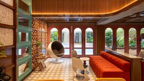 A spacious room with a checkered floor, a large window with multiple panes, a seating area with a red sofa, and a unique egg chair. - Miami Hotel (Bangkok)