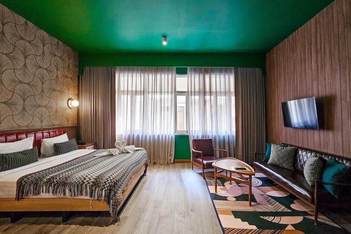 A hotel room with a bed, a sofa, a TV, and a window with curtains.