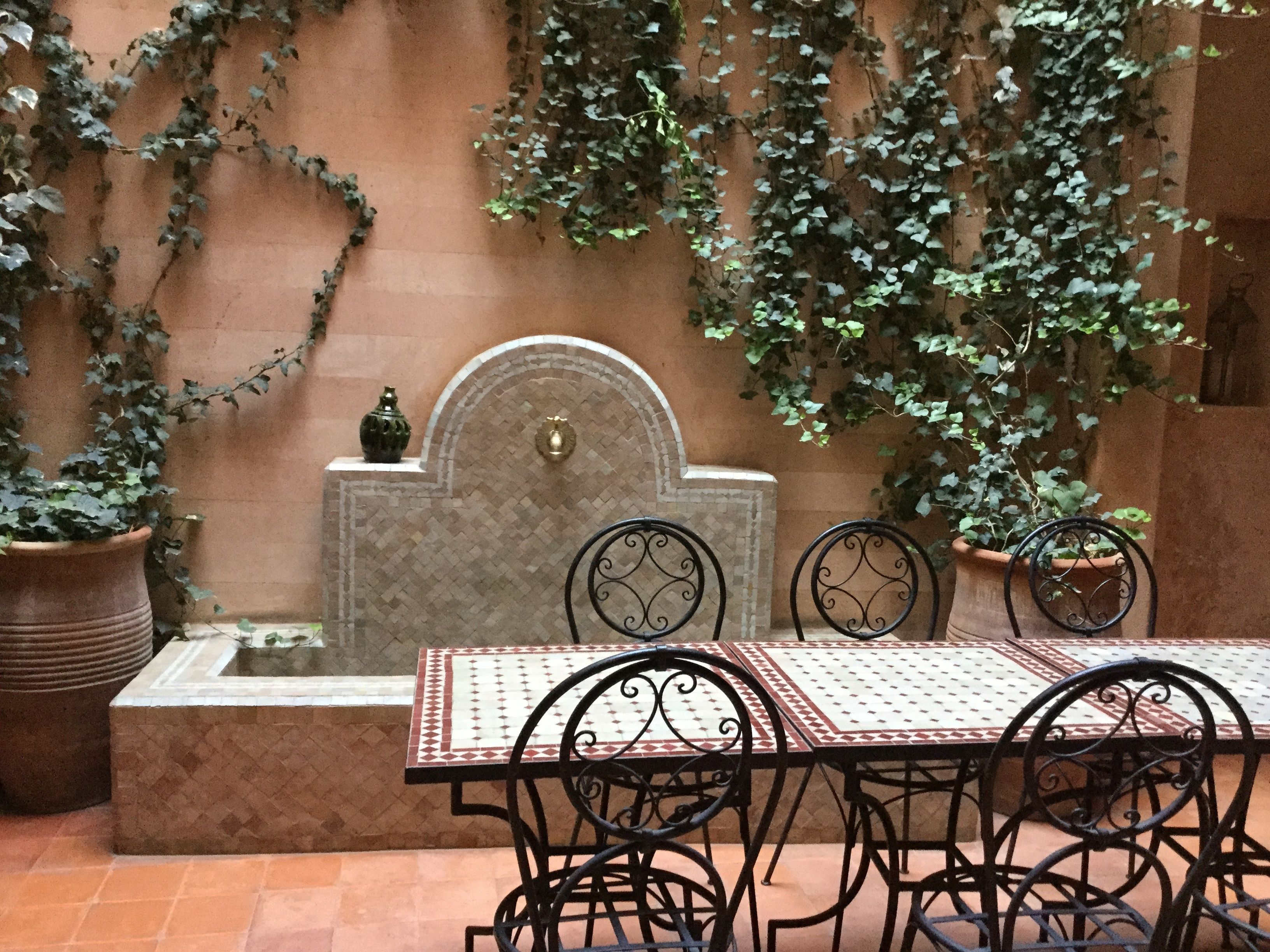 A patio with a tiled table and chairs, a decorative wall with plants, and a small fountain.